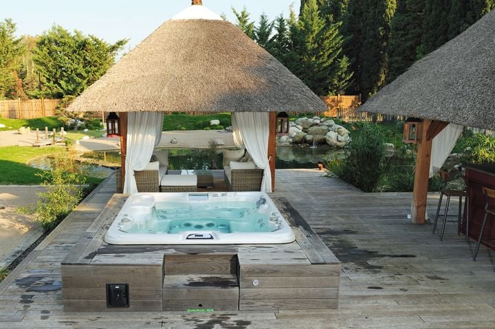 simple hot tub deck ideas - hot tub lowered into a deck with a gazebo and white curtains